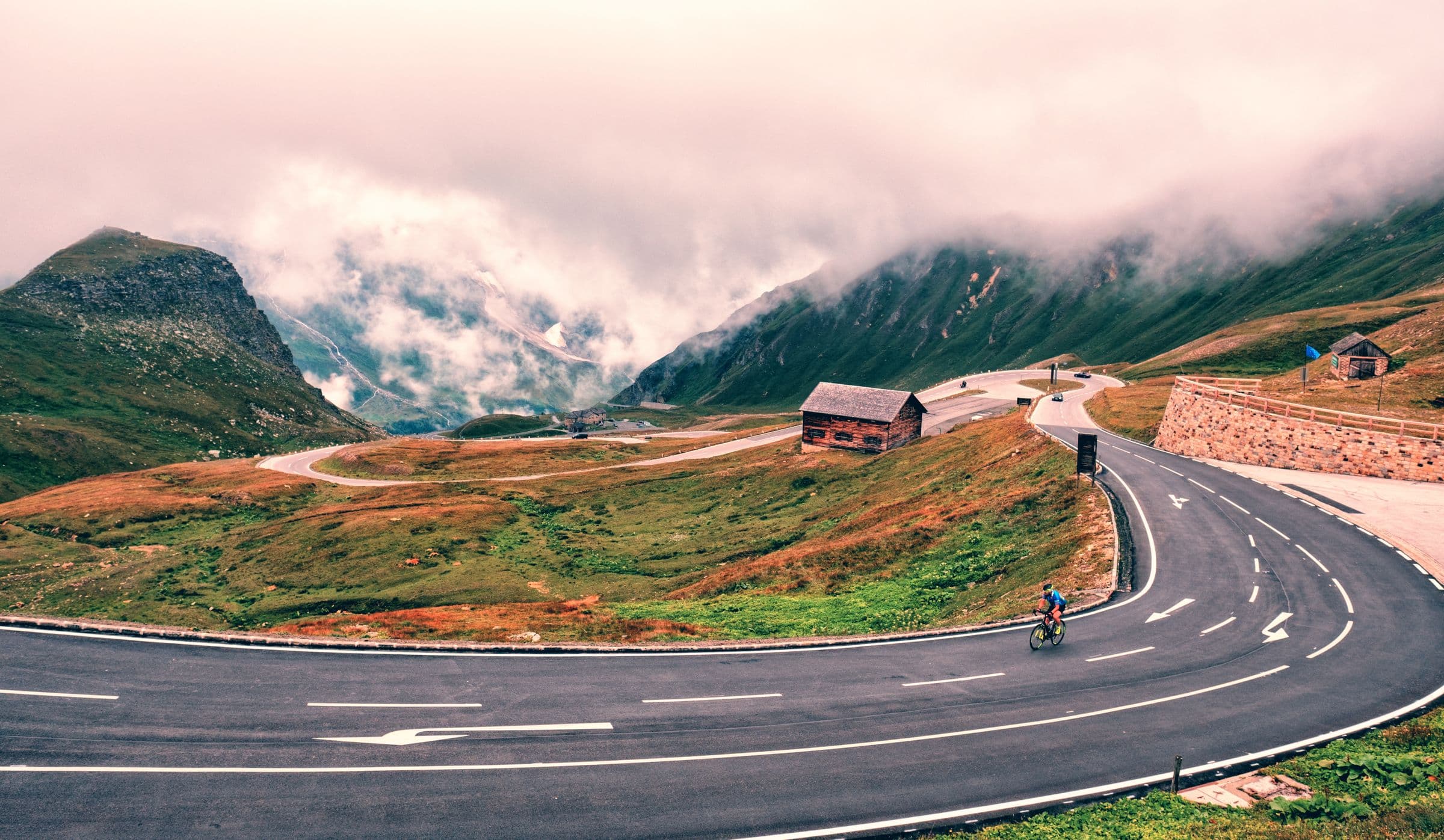 A lone road cyclist sweeping through an alpine switchback under low clouds