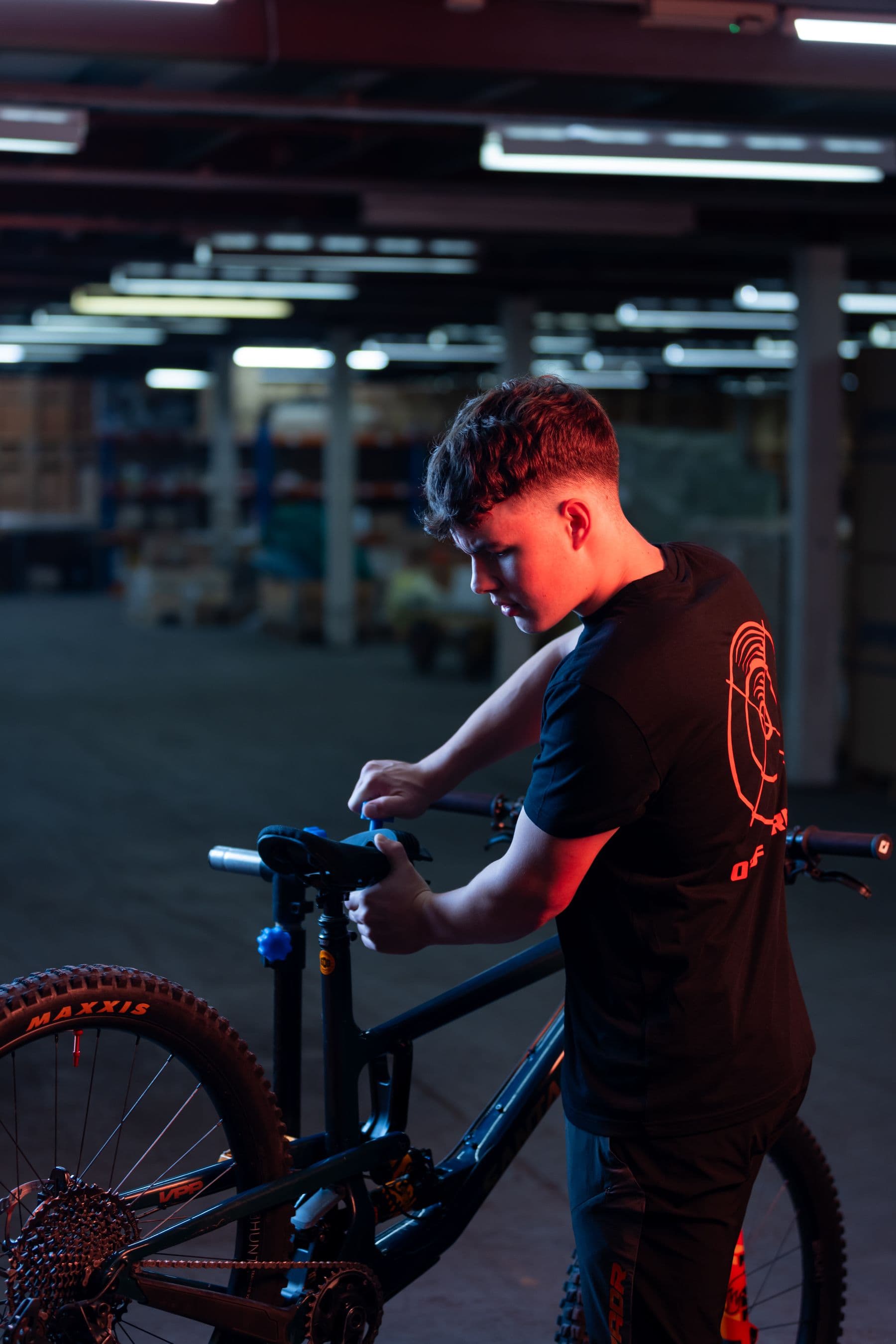 A mechanic adjusting the saddle of a mountain bike in a dark workshop lit with red rim light